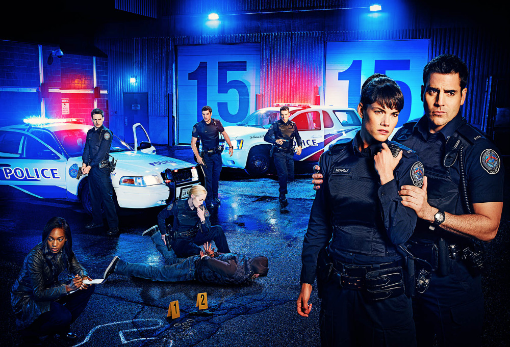 Police officers at an outdoor crime scene with police cars and evidence markers at night, with blue lighting and serious expressions.