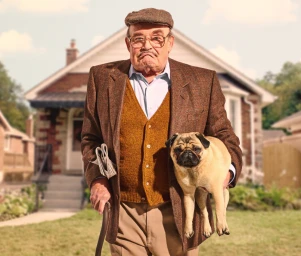 Elderly man holding a pug and a cane in front of a suburban house by Matt Barnes