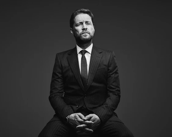 Monochrome portrait of a man in a pinstripe suit and tie seated against a dark background