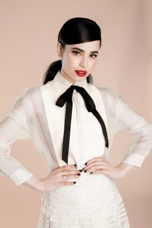 Portrait of Sofia Carson in a white blouse with a black bow and red lipstick against a neutral background by Brett Erickson.