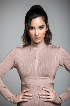 Headshot of an adult woman with a neutral expression, wearing a nude-colored dress, with her hands resting on her stomach.