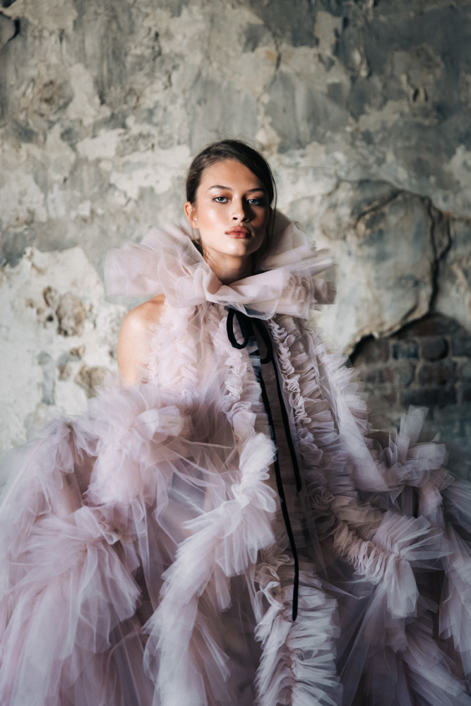 Woman in ruffled lilac tulle dress posing in photo studio with textured grey background, portrait style. Fashion shot, beauty concept.