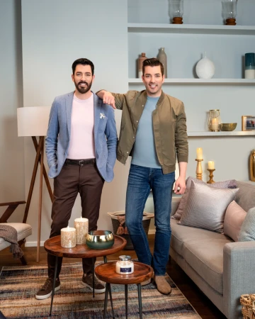 Two men standing in a living room interior with built-in shelves and a grey sofa, photographed by Brett Erickson.