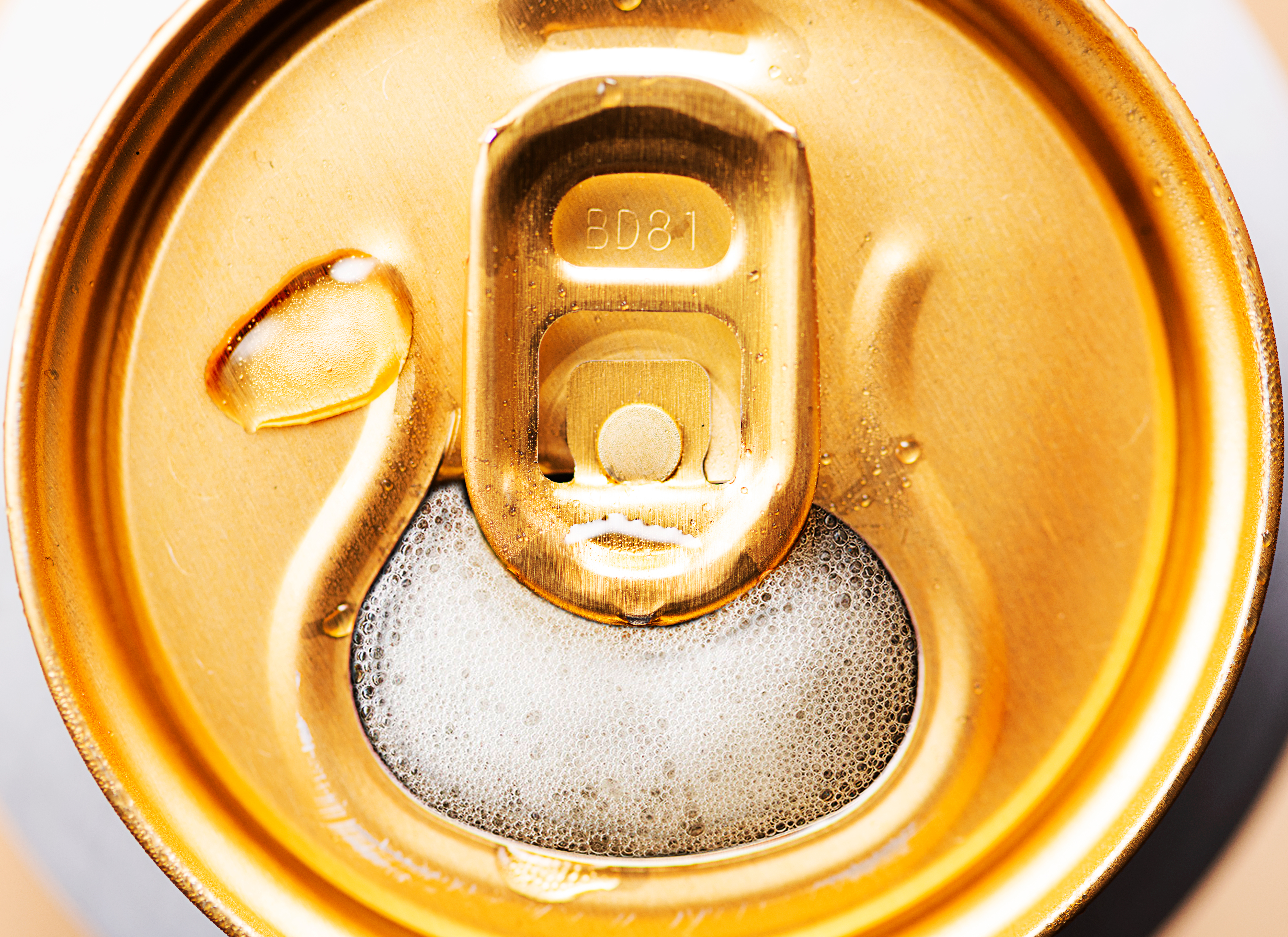 Close-up overhead shot of an open gold-colored aluminum can with a bubbly beverage inside, lit with bright studio lighting.
