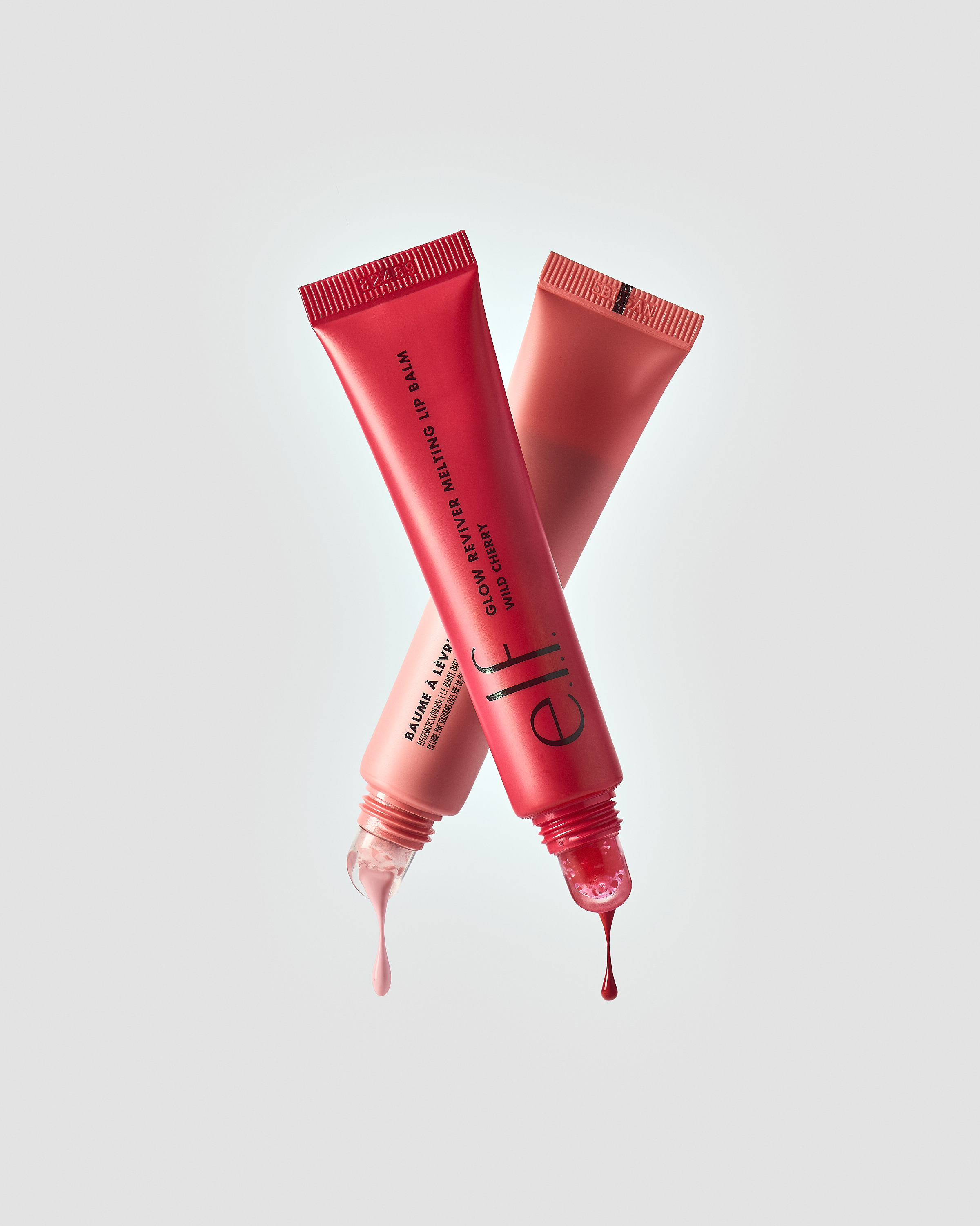 Two tubes of e.l.f. Glow Reviver Melting Lip Balm in red and pink are overlapping, product dripping from ends, isolated on grey.