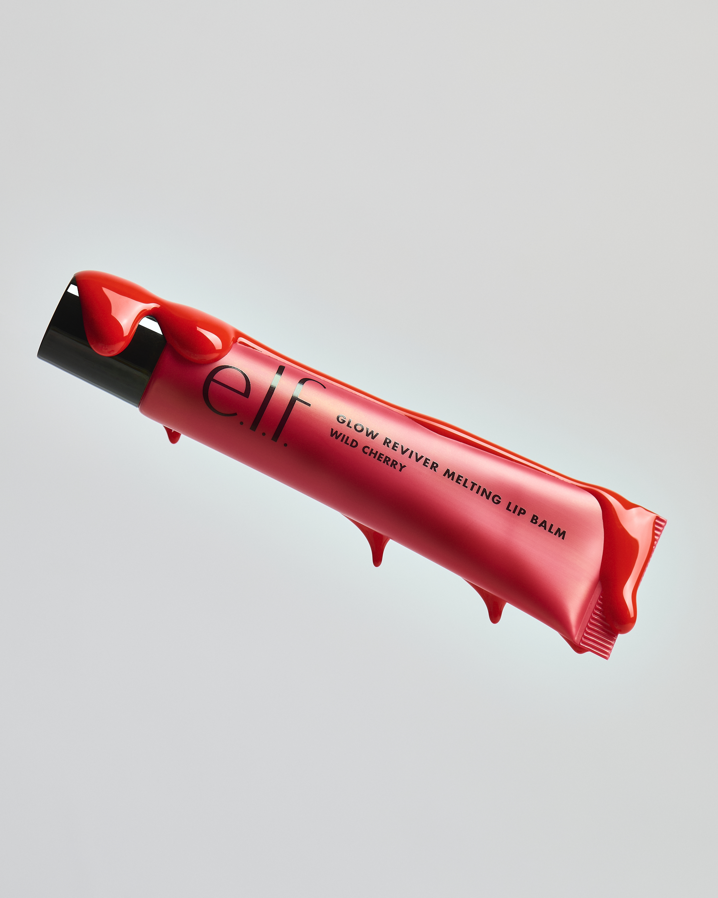 Floating red tube of e.l.f. Glow Reviver Melting Lip Balm with the product dripping down the tube in a studio product shot.