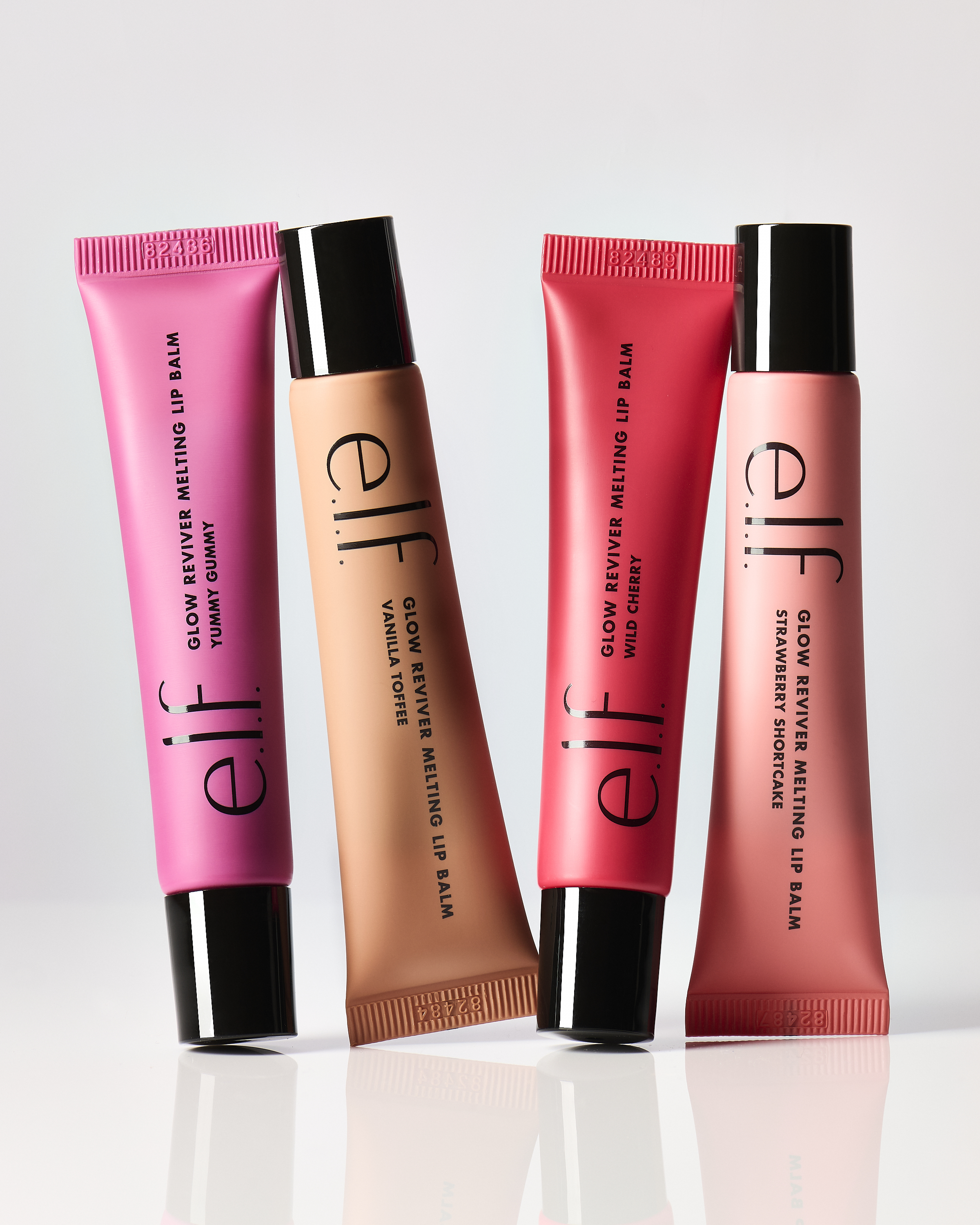 Four colorful tubes of ELF Glow Reviver Melting Lip Balm in pink, peach, and red tones against a neutral backdrop. Beauty product.