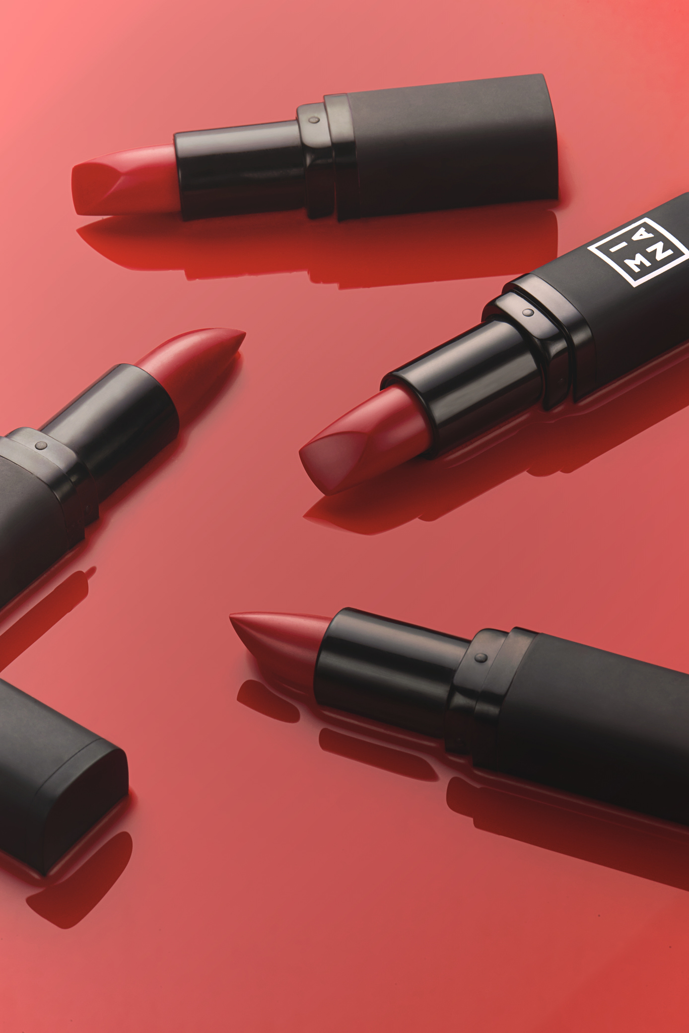 Overhead studio shot of four red lipsticks on a glossy red surface, creating a vivid and eye-catching beauty product still life.