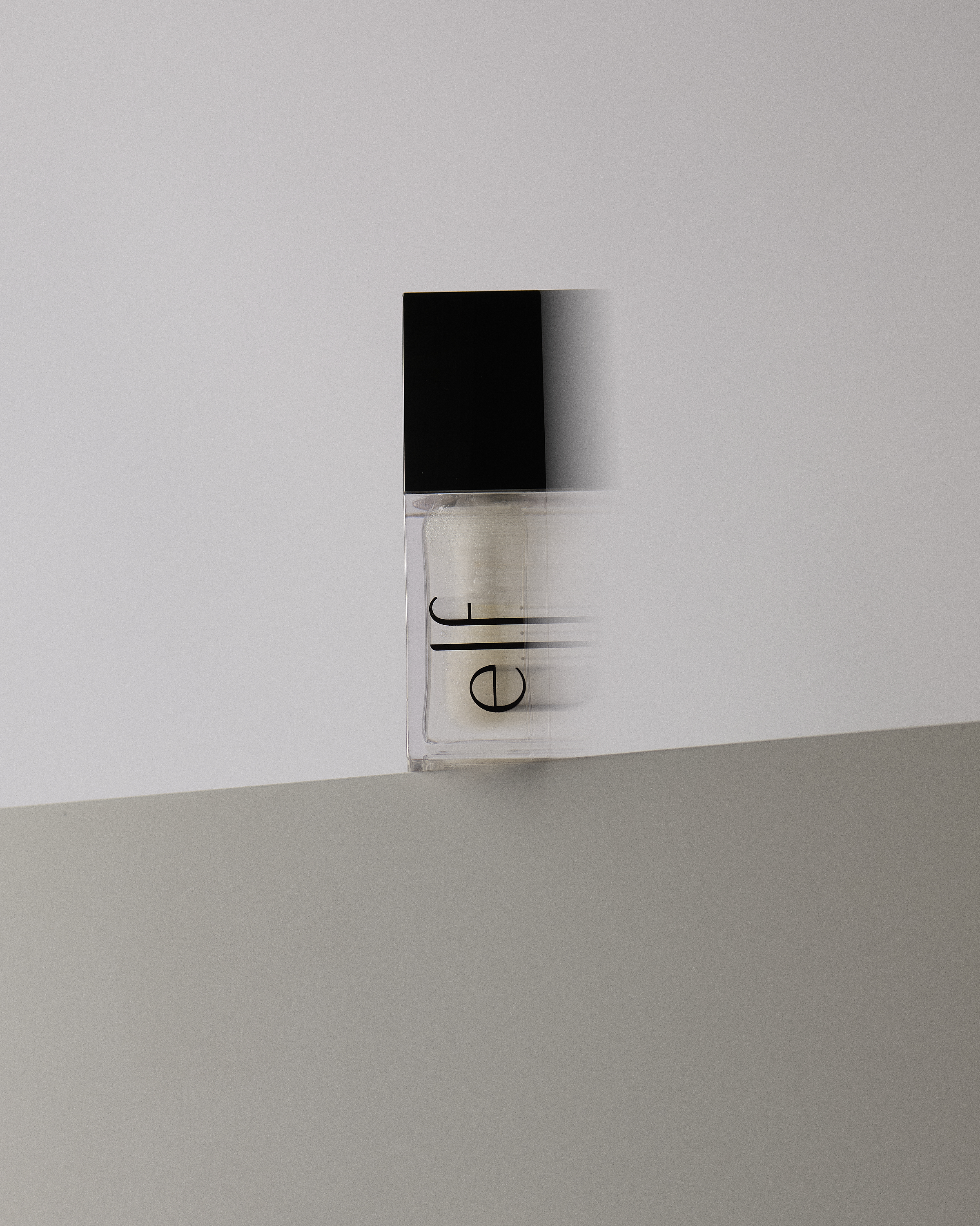 E.l.f. illuminating face powder with a black lid on a two-tone gray and white surface, close-up studio shot for beauty product.