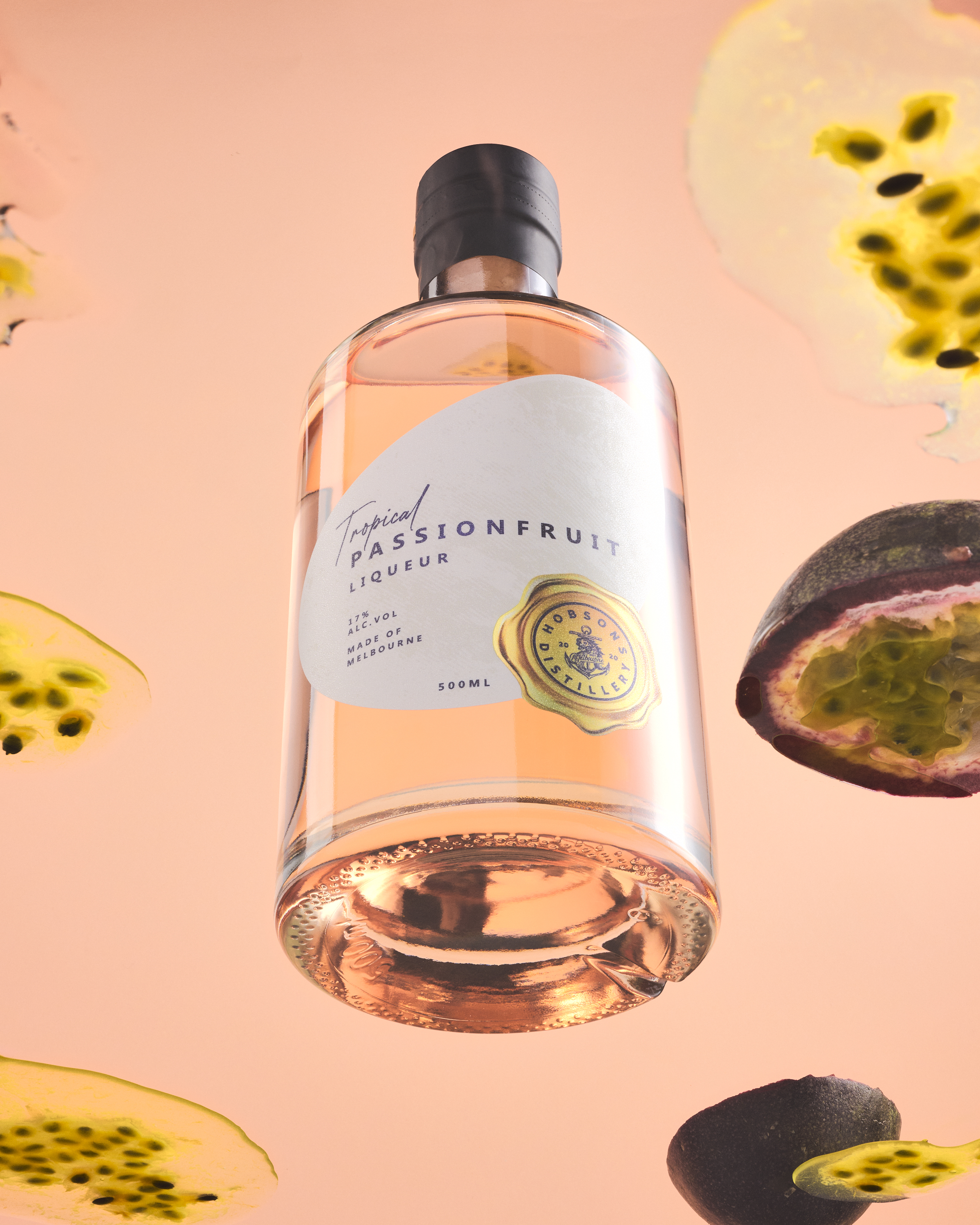 Product shot of passionfruit liqueur bottle with sliced passionfruits floating around it, set against a peach-colored background.