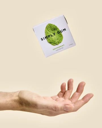 Package of peppermint chewing gum floating above a hand against a neutral background, product shot for food and beverage industry.