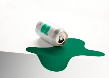 An open silver beverage can resting on its side atop a stylized green paper spill over the edge of a white surface.
