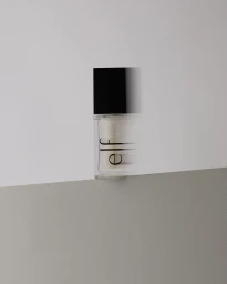 An e.l.f. cosmetic bottle with a black cap resting on an angled neutral grey surface with a horizontal motion blur effect.