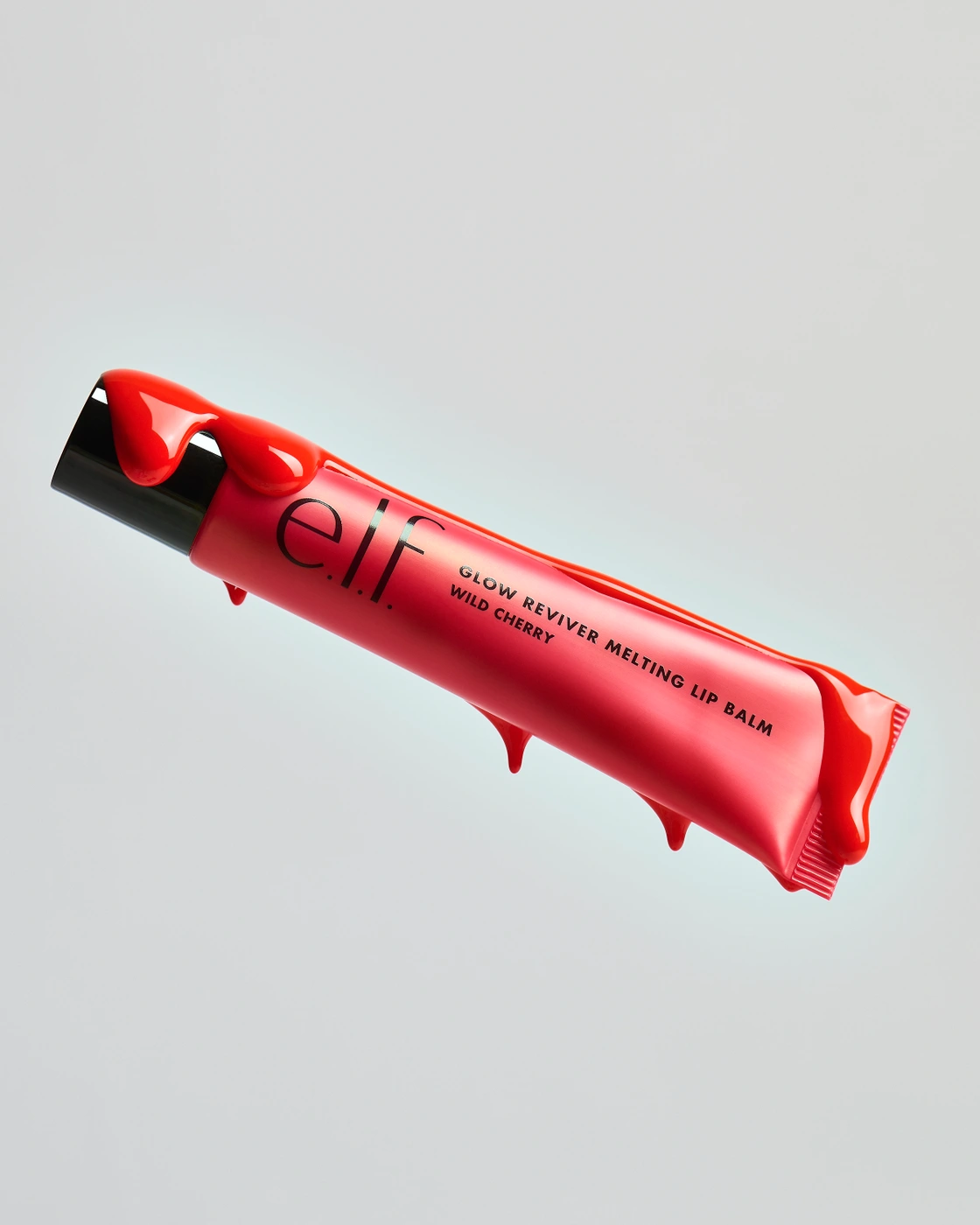 Floating tube of elf Glow Reviver Melting Lip Balm in Wild Cherry covered in dripping glossy red glaze against a light grey background.