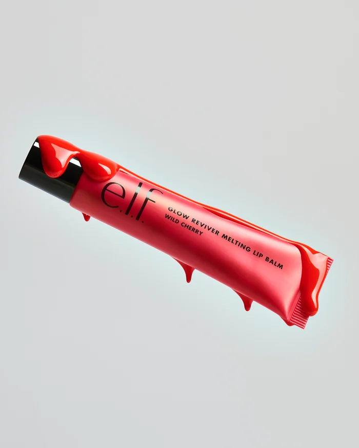 Floating tube of elf Glow Reviver Melting Lip Balm in Wild Cherry covered in dripping glossy red glaze against a light grey background.