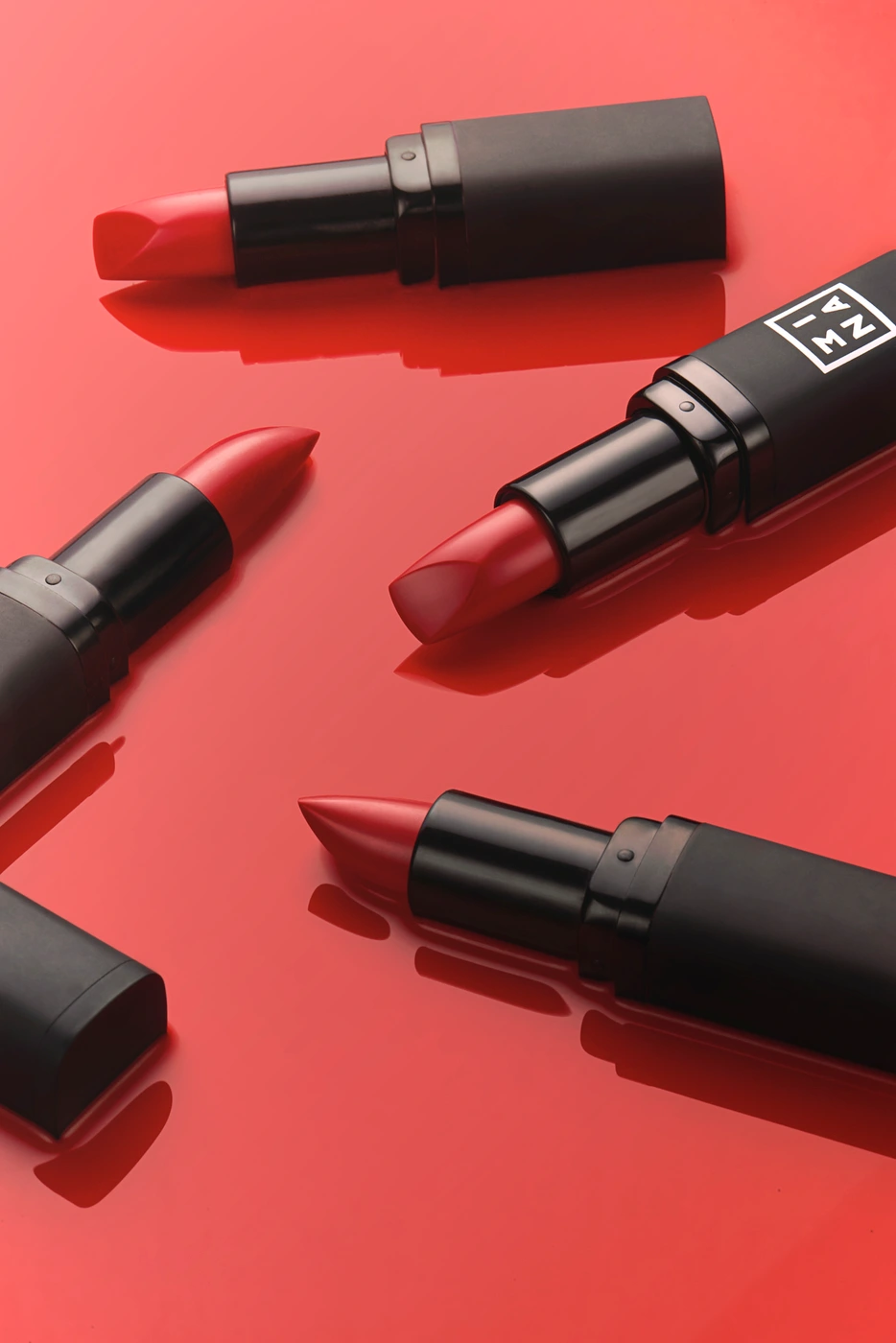 Red lipsticks in matte black casings arranged on a glossy reflective red surface.