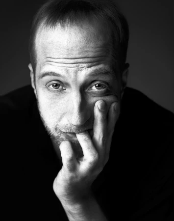 Close-up monochrome portrait of a white man in his 40s resting his hand against his face