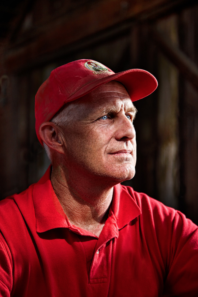 Portrait of a mature adult man wearing a red cap and polo shirt, looking up and away, indoors with a wood background.