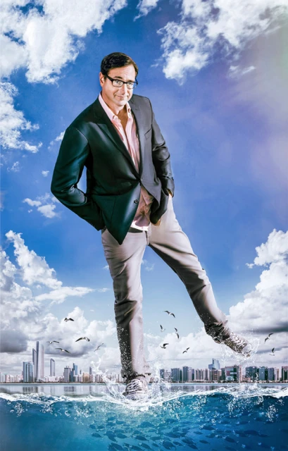 An adult male with glasses and a blazer poses, seeming to stride over a flooded city with a cloudy, blue sky in the background.