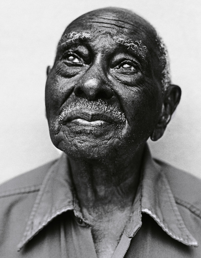 Black and white portrait of an elderly African-American man with wrinkled skin wearing a button-down shirt, looking up in contemplation.