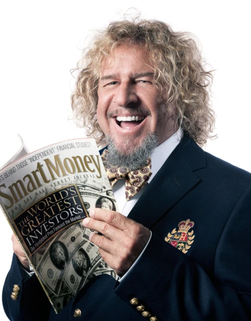 Adult male with curly hair, wearing a blazer and bow tie, smiles as he holds a magazine titled 'Smart Money' against a white backdrop.