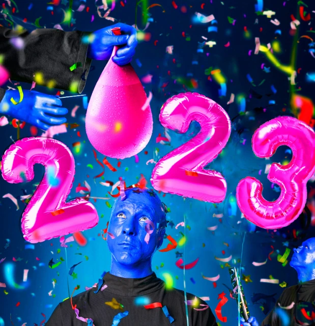 Whimsical New Year's image features a blue-skinned person surrounded by pink balloon numbers, confetti, and a water balloon ready to burst.