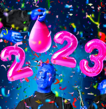 Whimsical New Year's image features a blue-skinned person surrounded by pink balloon numbers, confetti, and a water balloon ready to burst.