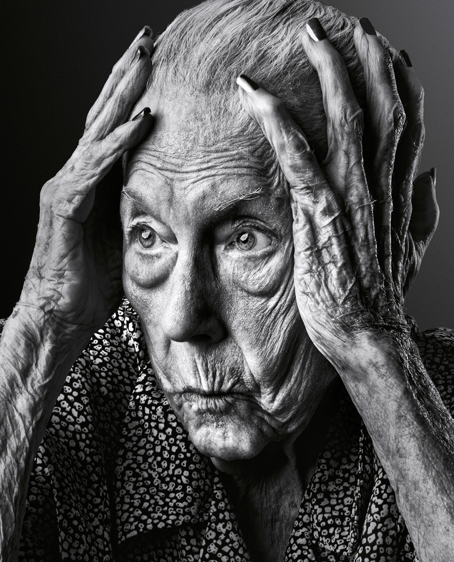Black and white portrait of an elderly woman with short gray hair, her hands framing her face, eyes looking to the side with worry.