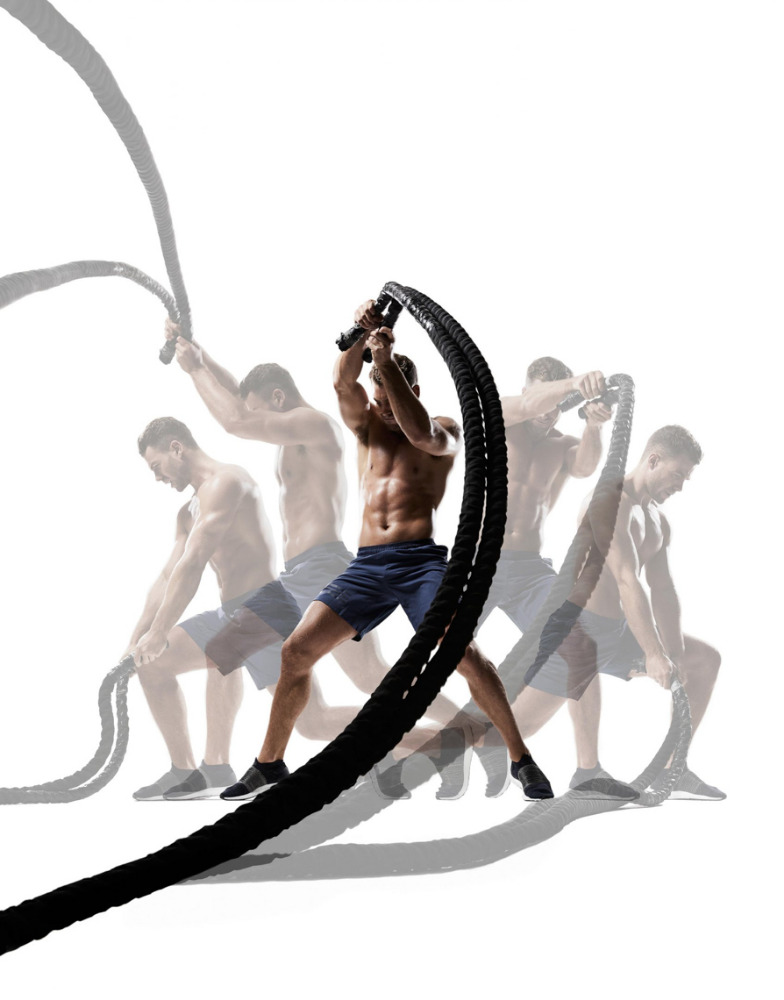 Muscular man in blue shorts exercising with battle ropes in a dynamic multiple exposure shot against a bright white background.