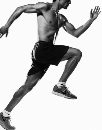 Muscular man running in athletic shorts and trainers against a bright white background in a black and white photograph