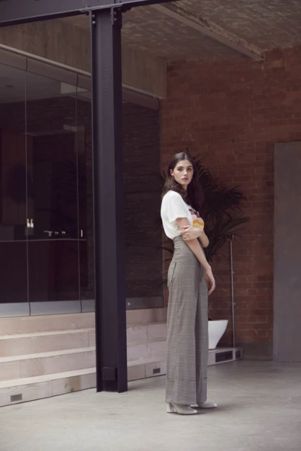 A full-length shot of a slender woman posing in an outdoor setting, wearing wide-leg pants and a white t-shirt in natural light.