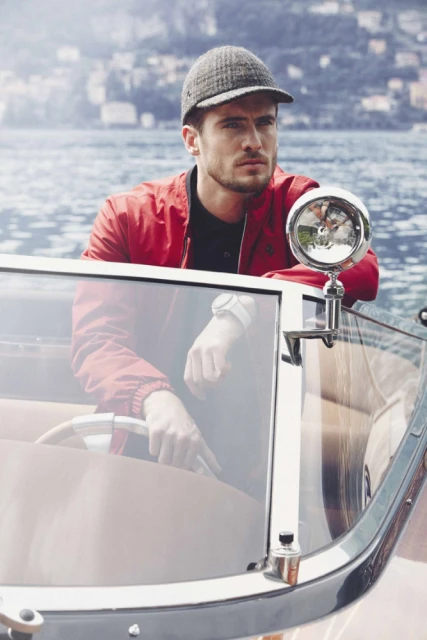Man in red jacket and cap on boat with lake and mountains background. Outdoor portrait capturing a relaxed moment on the water.