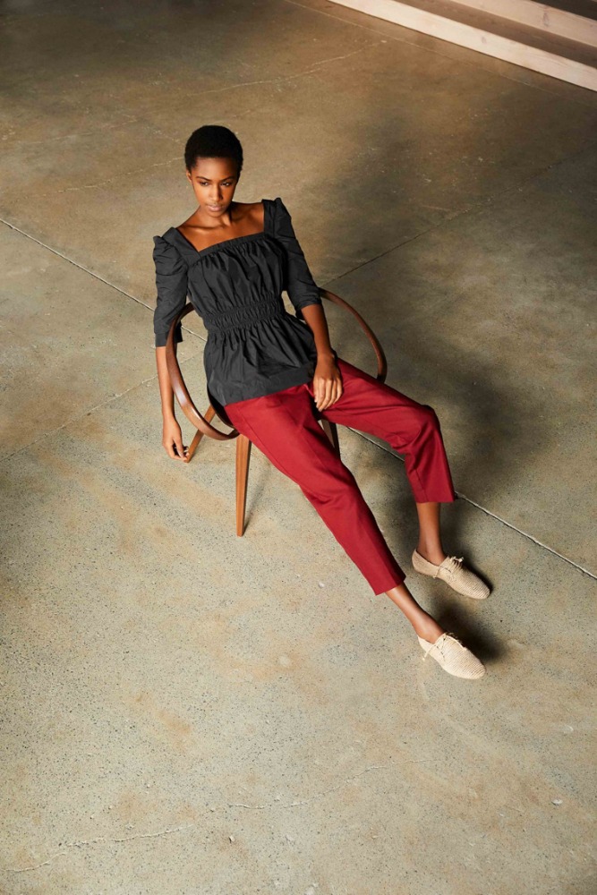 Fashion photo of an adult woman in a black top and red pants sitting on a chair in a studio with a concrete floor, shot from above.