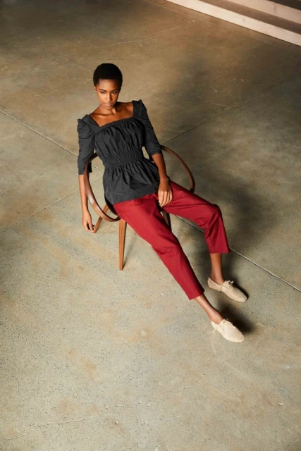 Fashion photo of an adult woman in a black top and red pants sitting on a chair in a studio with a concrete floor, shot from above.