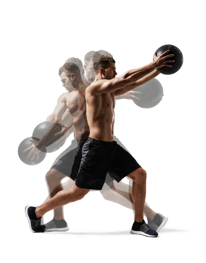 Athletic shirtless man performing medicine ball exercise with a motion blur effect on a white background in a fitness setting.