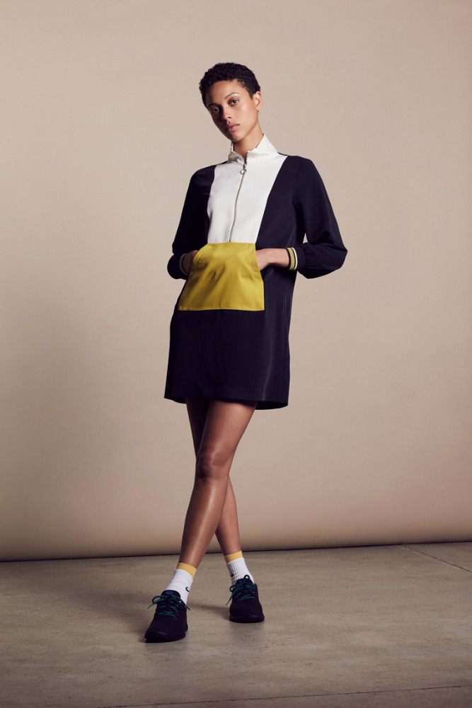 A stylish, short-haired woman poses in a color-blocked mini dress with sneakers and socks, set against a neutral studio backdrop.