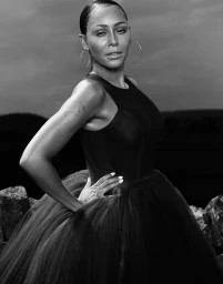 Black and white portrait of a woman in a dark dress with a voluminous tulle skirt and hoop earrings outdoors.