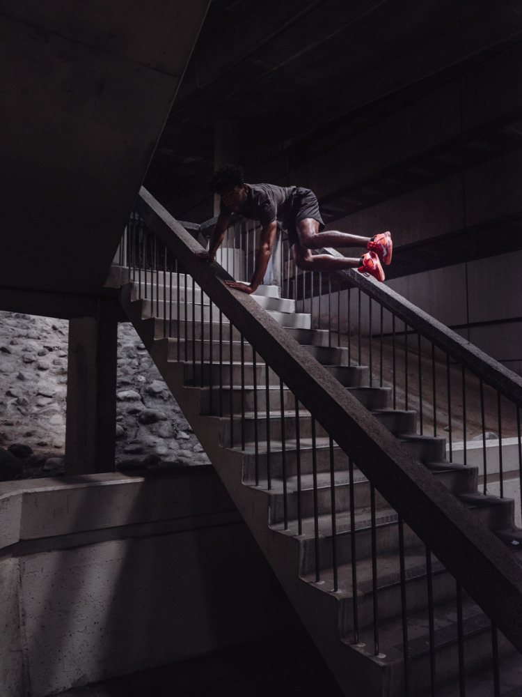 Athletic African-American male does a stair climber workout on concrete steps, wearing a gray shirt and red athletic shoes in an urban setting.