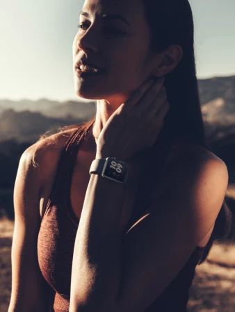Woman with an Apple Watch in a sporty top outside in a golden field with mountains in the distance, wearing a smart watch.