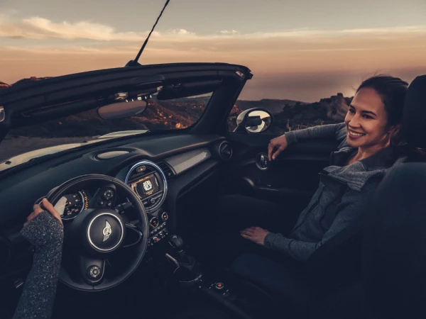 Convertible car ride at sunset featuring a woman passenger smiling and the driver's arm visible in the vehicle's interior.