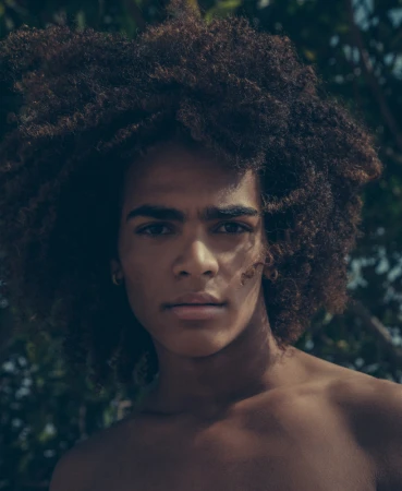Portrait of a young black man with voluminous curly dark hair outdoors with natural sunlight filtering through trees