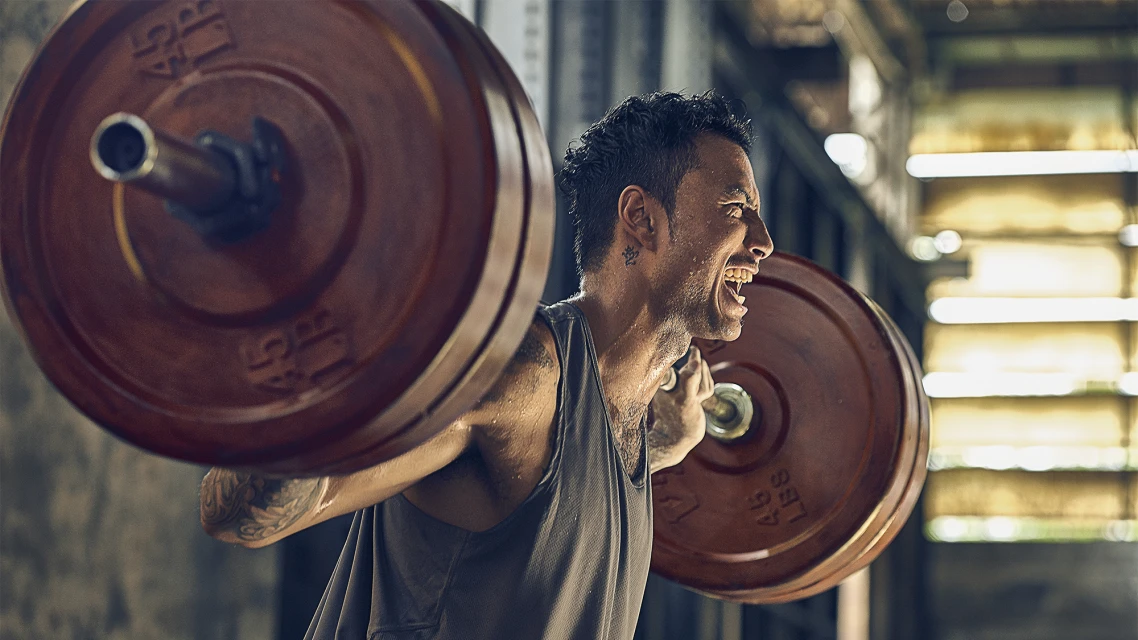 Athletic man with tattoos lifting heavy barbell in fitness center. Weightlifting exercise and workout routine for strength and muscle gain.