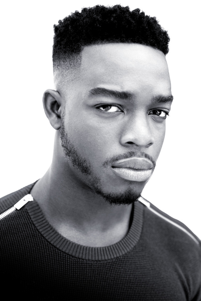 Striking black and white portrait of a young African-American man with a serious expression, close-cropped hair, and wearing a dark sweater.