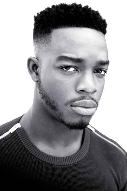 Striking black and white portrait of a young African-American man with a serious expression, close-cropped hair, and wearing a dark sweater.