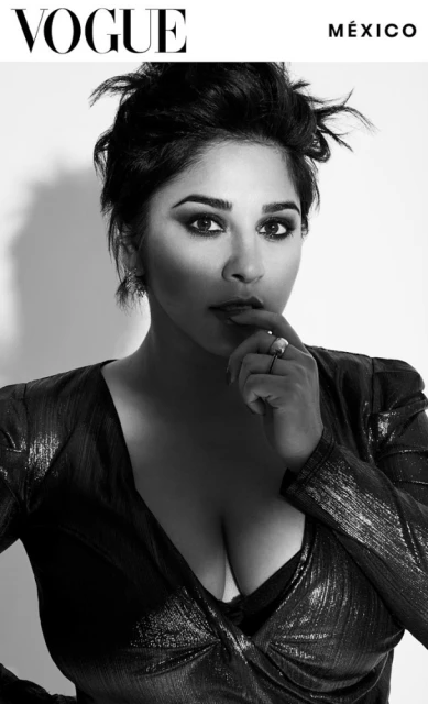 Black and white portrait of a woman with dark hair wearing a shimmery dress, posing in front of a white background with Vogue logo.