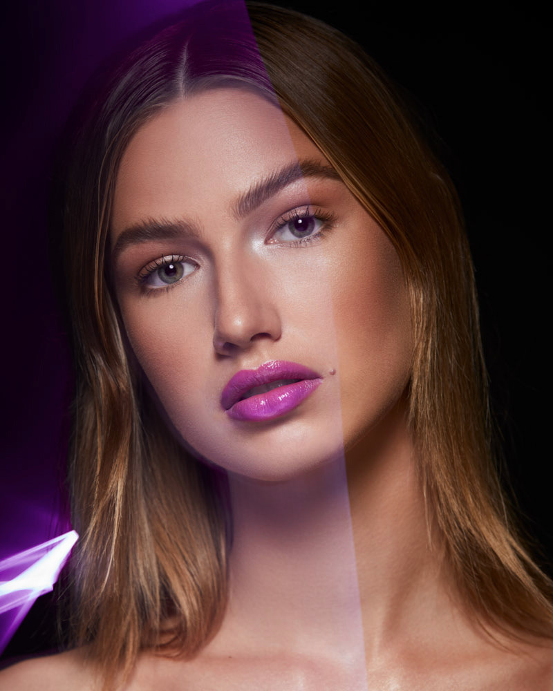 Close-up portrait of a young woman with fair skin and light brown hair, showcasing glossy pink lips in a studio setting with purple lighting.