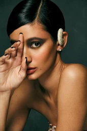 Close-up portrait of a woman with dark slicked-back hair, heavy eye makeup, and a textured ear cuff, photographed by Ryan West.