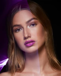 Close-up portrait of a woman with glossy purple lipstick against a dark background, photographed by Ryan West.