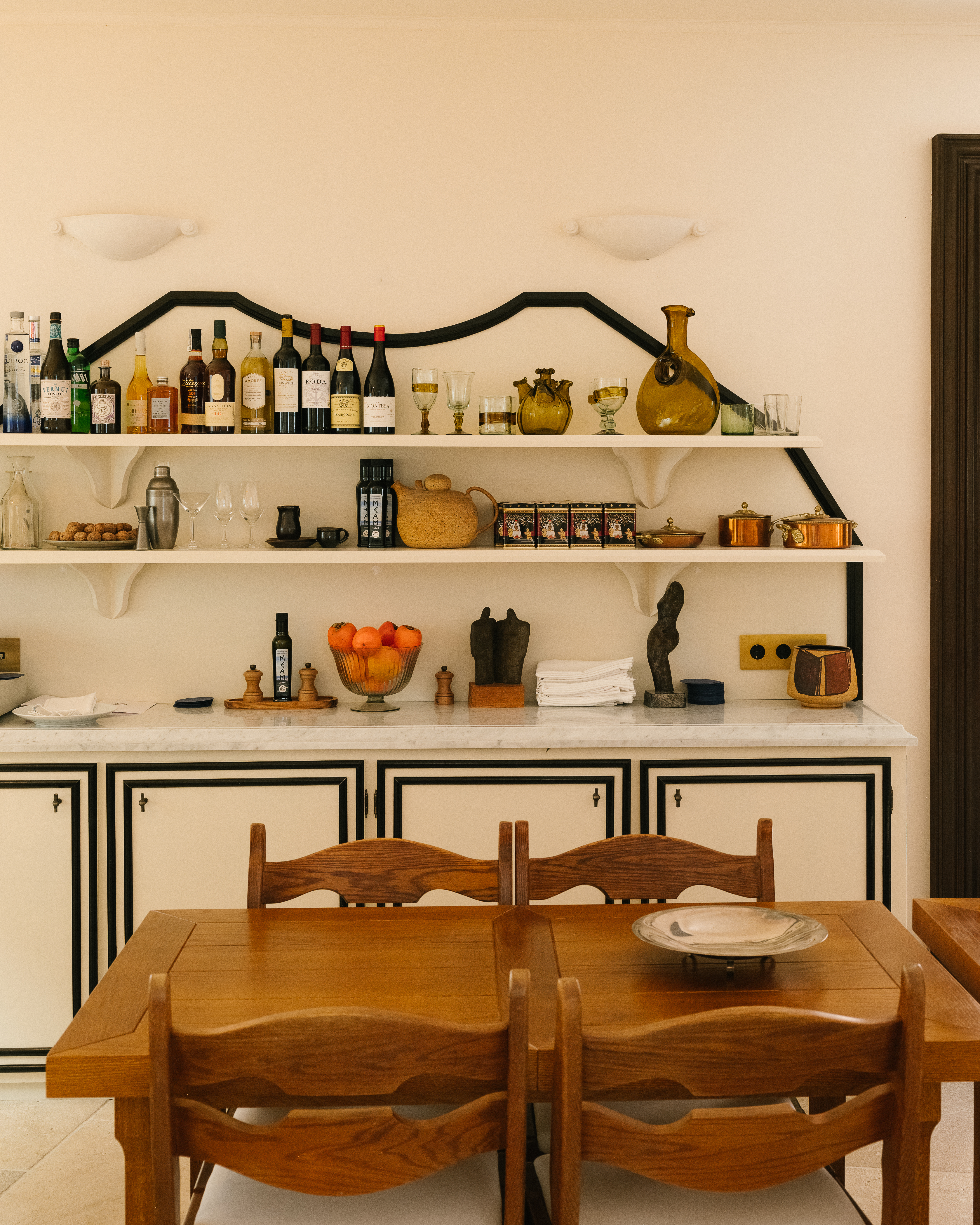 Indoor dining area featuring a wooden table and chairs, set against a backdrop of white cabinets and shelves displaying various decorative items.