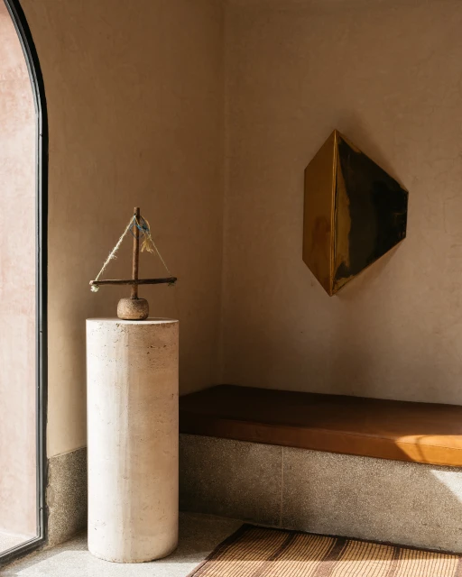 Interior view with decorative sailboat sculpture atop a cylindrical plinth, set against a backdrop of textured walls and modern art.